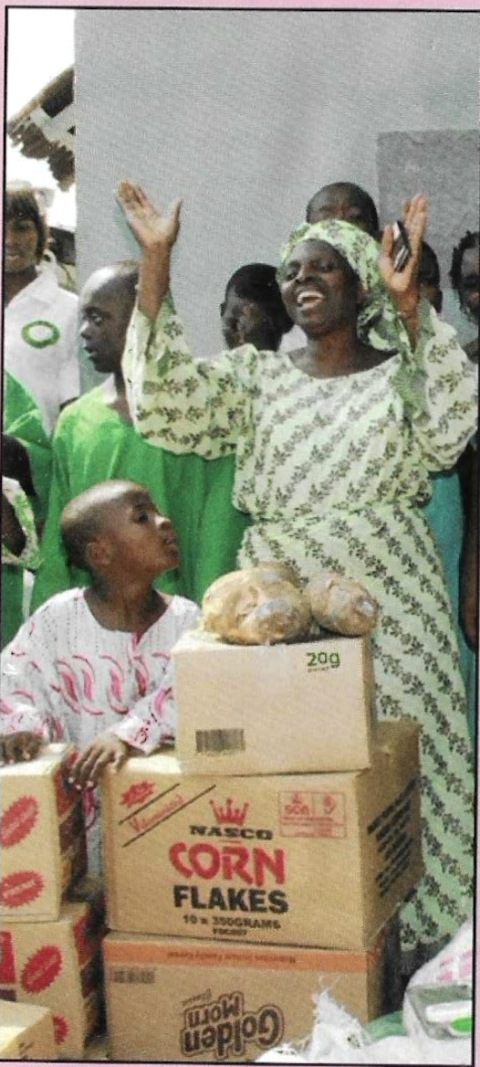 A beneficiary raising her hands in gratitude beside cartons of donated supplies