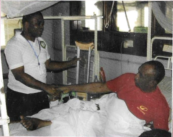 A KUTH volunteer greeting a patient at his hospital bedside during a medical outreach